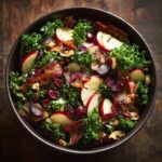 A vibrant bowl of Apple Cranberry Bacon Kale Salad with fresh ingredients and crispy bacon.