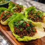 Close-up of Asian Ground Beef Lettuce Wraps on a wooden platter, garnished with cilantro and green onions.