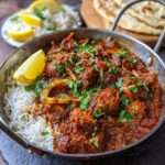 A serving of Authentic Chicken Curry Indian with rice, lemon, and naan bread. Garnished with cilantro.