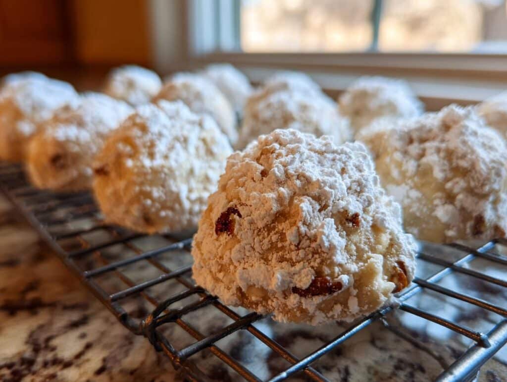 Freshly baked Buttery Pecan Snowballs dusted with powdered sugar, cooling on a wire rack.