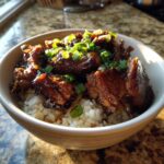 A bowl of Caramelised Soy Chicken in Garlic Ginger Broth with Rice, garnished with green onions.