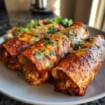 Three chicken enchiladas covered in red sauce and cheese, garnished with cilantro, on a white plate. Chicken Enchiladas Recipe.