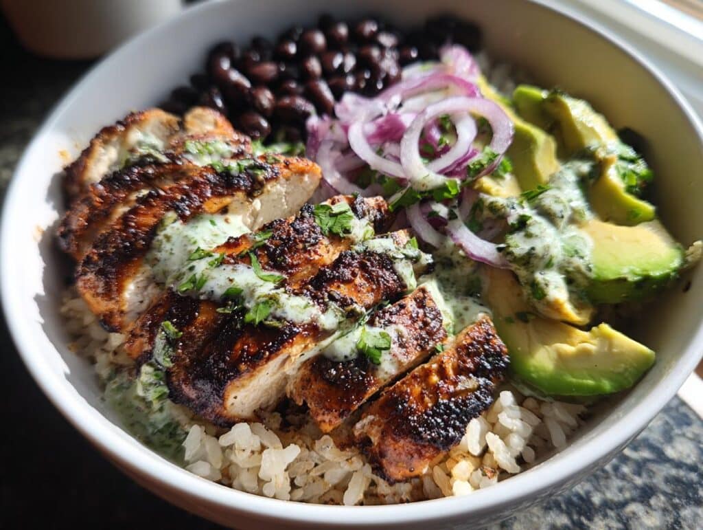 A vibrant Chimichurri Grilled Chicken Bowl with Garlic Sauce, featuring grilled chicken, rice, beans, avocado, and red onions.