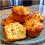 A stack of golden Cottage Cheese Blender Muffins on a blue plate, one muffin broken open.