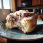 A single Creamy Bueno Cinnamon-Style Roll with a bite taken out, sits on a blue plate with icing dripping down.