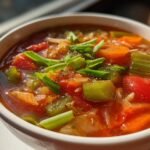 A close-up of a bowl of Detox Cabbage Soup, filled with colorful vegetables and garnished with fresh herbs.