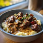 A bowl of easy beef tips with creamy mushroom gravy served over mashed potatoes, garnished with fresh thyme.
