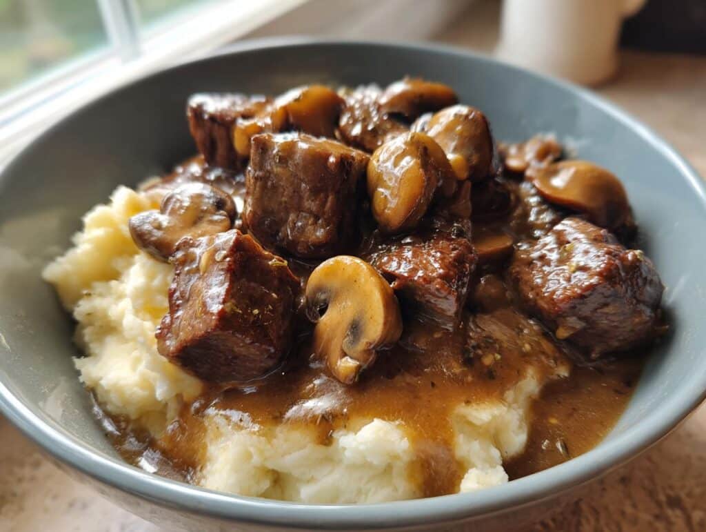 A bowl of Easy Beef Tips with Creamy Mushroom Gravy over mashed potatoes.