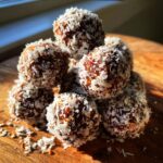 A stack of Easy No-Bake Peppermint Balls coated in shredded coconut, sitting on a wooden board.