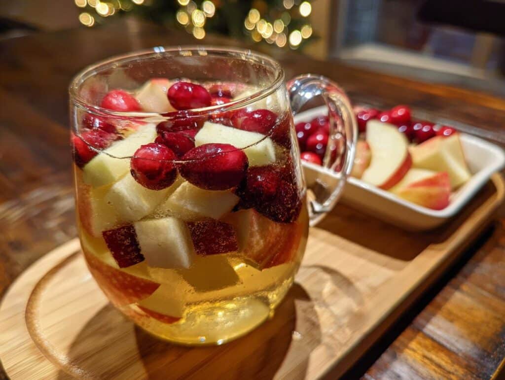 Festive White Christmas Sangria in a glass mug with cranberries and apples, served on a wooden tray.