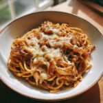 A bowl of French Onion Soup Pasta with Gruyere cheese melted on top, ready to eat.