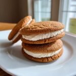 A stack of three Ginger Molasses Sandwich Cookies with creamy filling on a white plate.