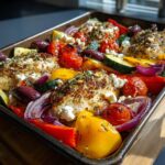A sheet pan filled with Greek Sheet Pan Feta Chicken and Veggies, including chicken, feta, peppers, zucchini, olives, and tomatoes.