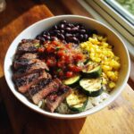 A vibrant Grilled Steak Bowl with Sauce & Grilled Zucchini, featuring steak, rice, beans, corn, and salsa.