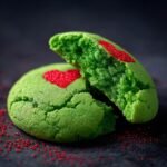 Close-up of a halved green Grinch Sugar Cookie with a red heart decoration, revealing its soft texture.