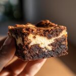 Close-up of a Healthier Cream Cheese Swirl Brownie slice being held, showing the swirl and texture.