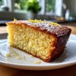 A delicious slice of Healthier Lemon Olive Oil Cake on a white plate, garnished with lemon zest.