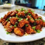 Close-up of Healthy Orange Chicken pieces on a white plate, garnished with green onions.