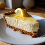 A delicious slice of Lemon Cheesecake Tart with a graham cracker crust, lemon zest, and a lemon wedge.