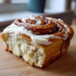 A single, delicious Lotus Biscoff Cinnamon Roll topped with creamy white icing, sitting on a wooden surface.
