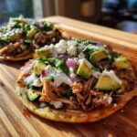 Two Mexican Rotisserie Chicken Tostadas with Zucchini, avocado, red onion, cilantro, and cheese on a wooden board.