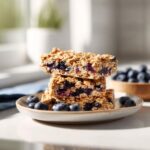 A stack of three No Bake Blueberry Oat Bars on a plate, surrounded by fresh blueberries.