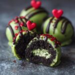 A cut-open No-Bake Grinch Oreo Truffle showing the Oreo filling and green coating, with red heart sprinkles.