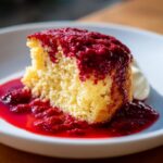 A slice of Red Velvet Self Saucing Pudding with sauce and cream on a plate.