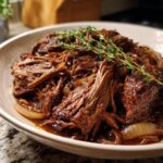 A bowl of Slow Cooker French Onion Pot Roast, garnished with thyme, showcasing tender beef and caramelized onions.