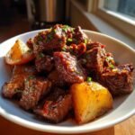 Close-up of Slow Cooker Garlic Butter Beef Bites & Potatoes in a white bowl, garnished with herbs.