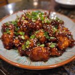 A plate of delicious Sticky Honey Gochujang Chicken, garnished with sesame seeds and green onions.