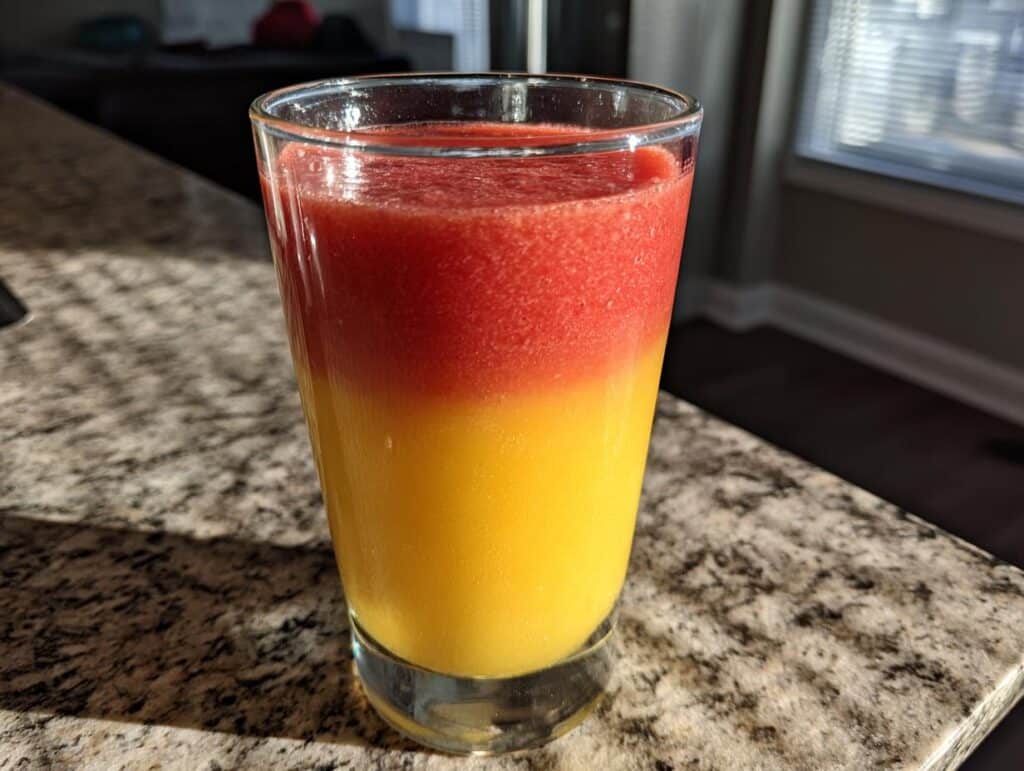 A glass of Refreshing Sunrise Sunset Smoothie Recipe with red and yellow layers.