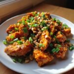 A plate of Thai Peanut Chicken, garnished with chopped peanuts and green onions.