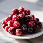 A pile of glistening Traditional Sugared Cranberries on a white plate, ready to eat.