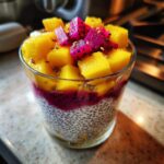 A glass of Tropical Mango & Dragon Fruit Chia Pudding with layers of chia seeds, dragon fruit puree, mango and dragon fruit chunks.