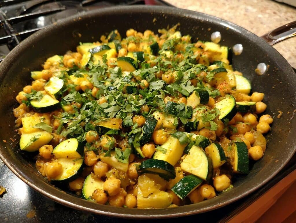 A freshly cooked Zucchini and Chickpea Skillet, garnished with fresh herbs, in a dark skillet.