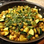 A freshly cooked Zucchini and Chickpea Skillet, garnished with fresh herbs, in a dark skillet.