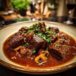A bowl of Anthony Bourdain’s Beef Bourguignon, garnished with fresh parsley and served with mushrooms.