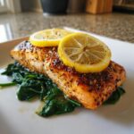 A perfectly cooked piece of Baked Salmon with Spinach, topped with two lemon slices, on a white plate.