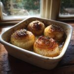 Four baked Tennessee Onions in a white baking dish, garnished with herbs, sitting on a wooden surface.