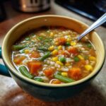 Close-up of a bowl of hearty Vegetable Soup with carrots, green beans, corn, and peas.
