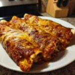 Three delicious Chicken Enchiladas covered in red sauce and melted cheese on a white plate.
