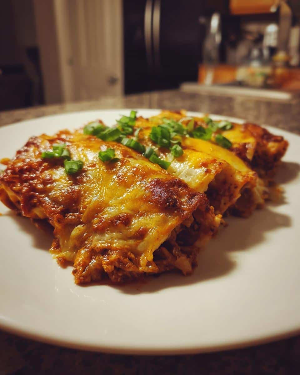 Irresistible Chicken Enchiladas in Under 60 Minutes 7 Three cheesy Chicken Enchiladas on a white plate, garnished with green onions. Ready to eat!