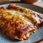 Two Chicken Enchiladas with Sour Cream Sauce, topped with melted cheese, on a plate.
