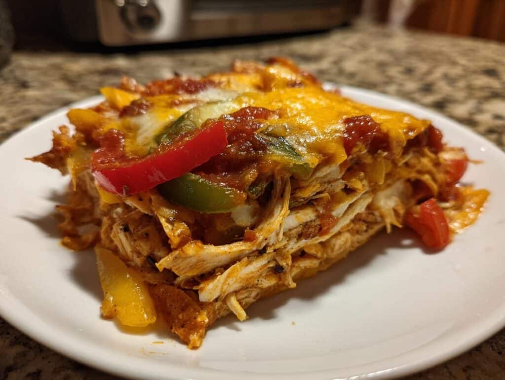 A slice of Chicken Fajita Casserole with chicken, peppers, cheese, and salsa on a white plate.