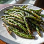 A plate of crispy Crack Green Beans, lightly charred and sprinkled with parmesan cheese.