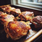 Close-up of several Crispy Baked Chicken Thighs with golden-brown skin on a baking sheet.