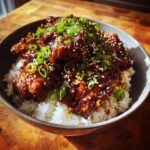 A bowl of Crock Pot Bourbon Chicken served over white rice, garnished with sesame seeds and green onions.