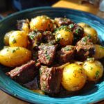 A bowl of Crockpot Garlic Butter Beef Bites with Potatoes, garnished with fresh herbs.