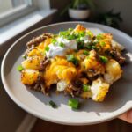 A plate of Crockpot Loaded Steak Potato Bake topped with sour cream and green onions.